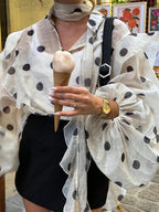 Une blouse semi-transparent en mousseline, couleur crème imprimée de grands pois noirs.